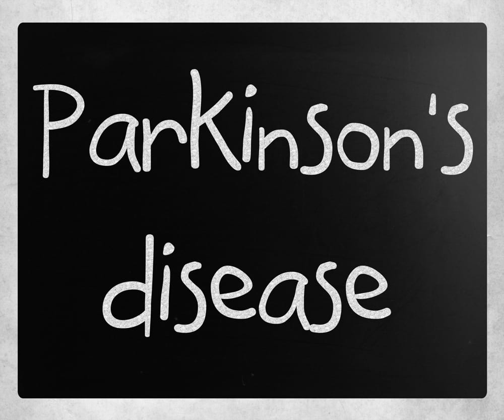 An illustration of the words Parkinson's Disease handwritten in white chalk on a black chalkboard with a silver border