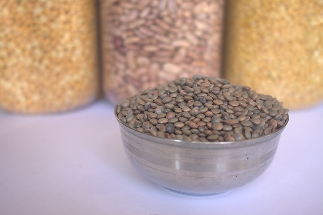 A bowl of lentils set in front of three jars of other legumes.