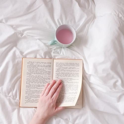 Book and cup of tea on a bed.