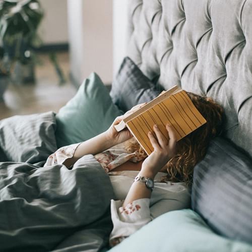 Woman lying down in bed with a book over her face.