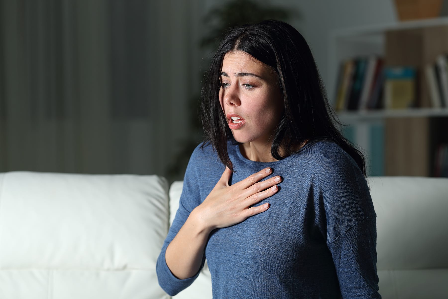 Woman sitting on couch with hand on her chest suffering from an Anxiety attack.