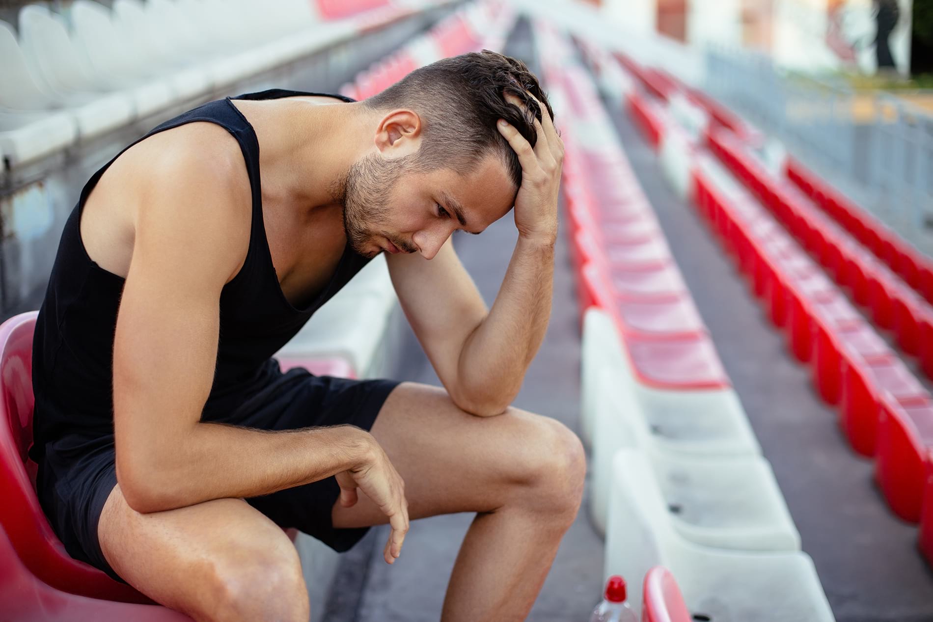 Male athlete sitting down in bleachers looking upset and in need of some sports psychology.