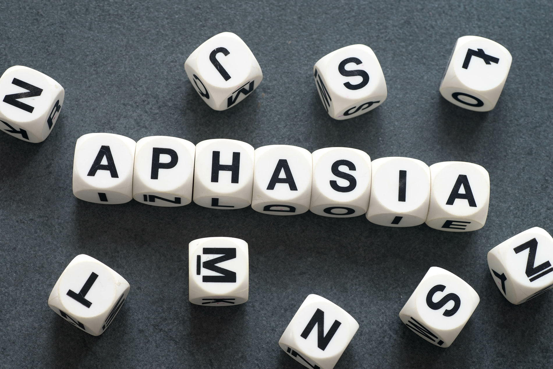 Aphasia spelled out in dice with jumbled letters around it.